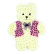 A three-dimensional floral teddy bear stands centered against a plain white background, a gentle and touching tribute crafted entirely from fresh blooms. The entire figure-from the soft curve of its ears to the rounded paws-is densely covered in creamy white chrysanthemums, arranged so closely that they create the illusion of plush, velvety fur. The petals form a smooth, continuous surface over the bear's head, body, arms, and legs, giving it a cuddly, toy-like shape that feels instantly familiar and comforting. Dark floral accents are used sparingly to mark out two bright eyes and a neat little nose, giving the teddy a kind, slightly wistful expression that suggests both innocence and quiet strength. Draped smartly across its chest is a waistcoat made from rich purple and mauve flowers, clearly shaped with lapels and front panels that contrast beautifully against the pale fur. At the neckline, a bow of fine lavender mesh is tied neatly, its light, airy loops catching the light and adding a soft, decorative flourish. As a florist working with families in Queensbury and the nearby streets off Kingsbury Road, I often see this design chosen as a deeply personal sympathy tribute, especially when saying goodbye to a child or someone remembered for their gentle spirit. The arrangement conveys a sense of warmth, compassion, and cherished memories, making it a meaningful choice for funeral services, memorials, or quiet gatherings at home, where the presence of this floral teddy brings a subtle, consoling grace.